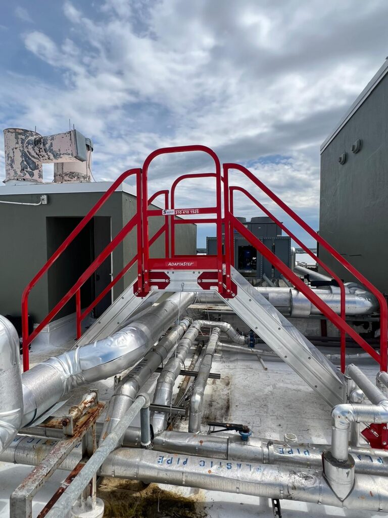 AdaptaStep access platform with red railings around industrial pipework.
